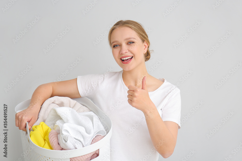 Young woman with laundry showing thumb-up gesture on grey background