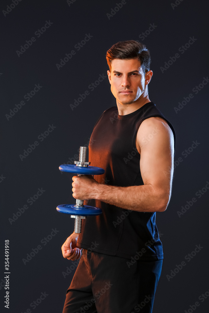 Sporty young man with dumbbell on dark background