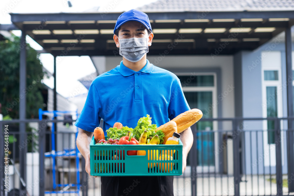 亚洲送货员身穿蓝色制服，戴着医用口罩，为杂货店提供新鲜食品t