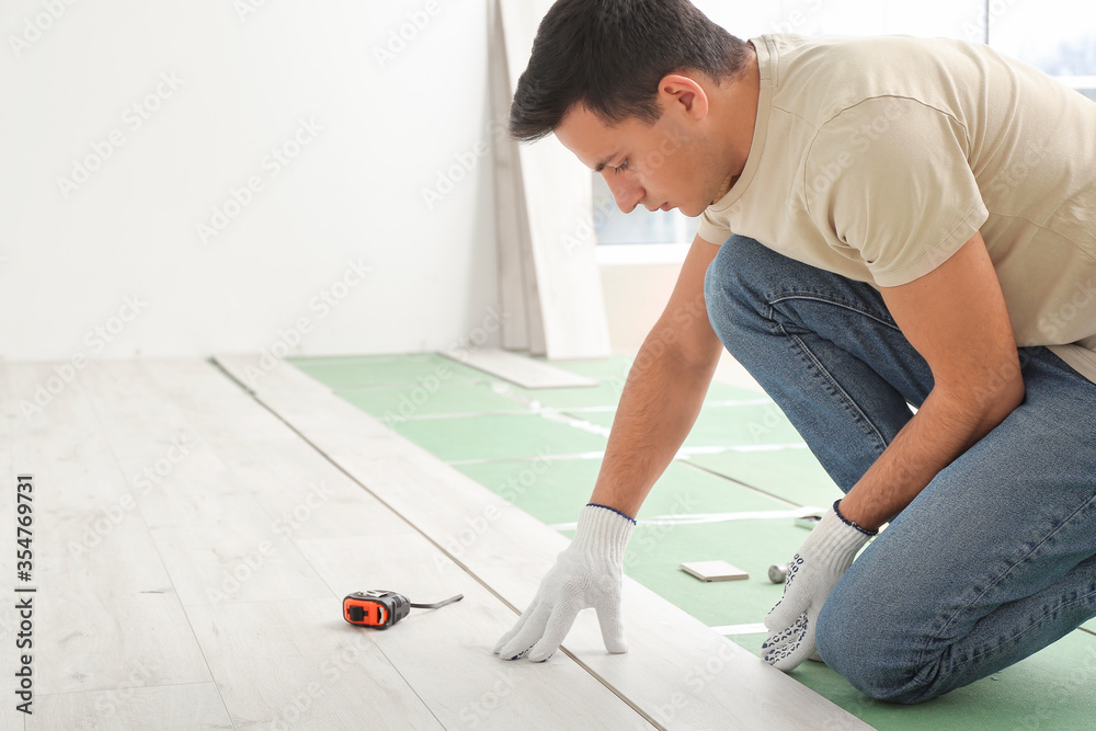 Carpenter installing laminate flooring in room