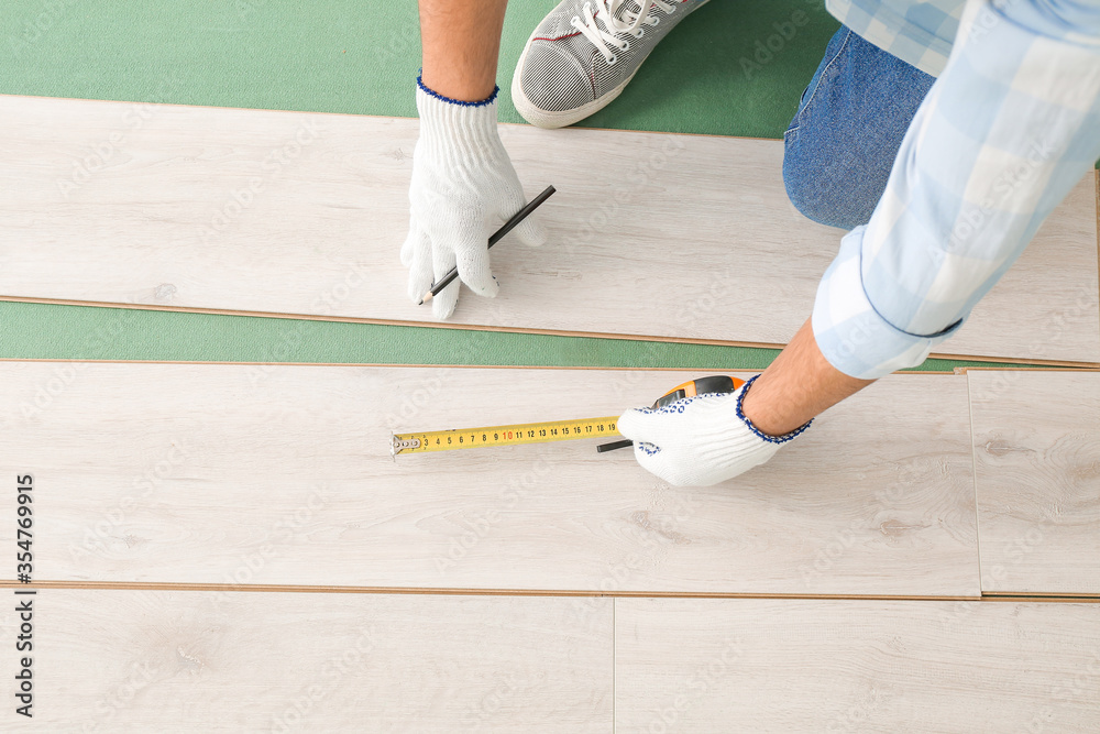 Carpenter installing laminate flooring in room