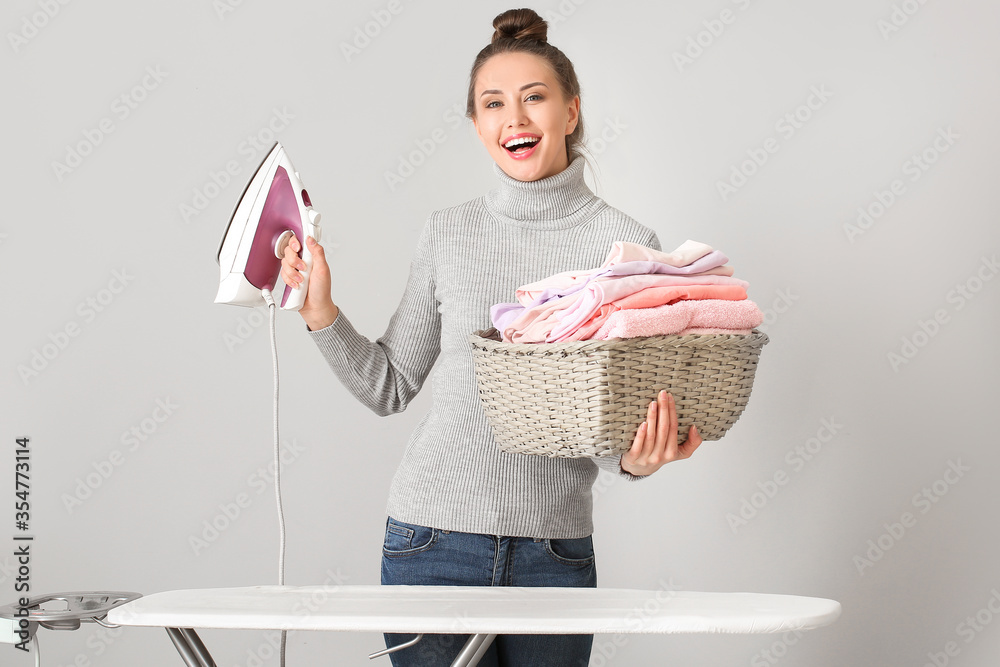 Young woman ironing laundry on grey background