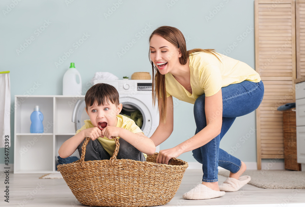 Young woman with her little son having fun while doing laundry at home