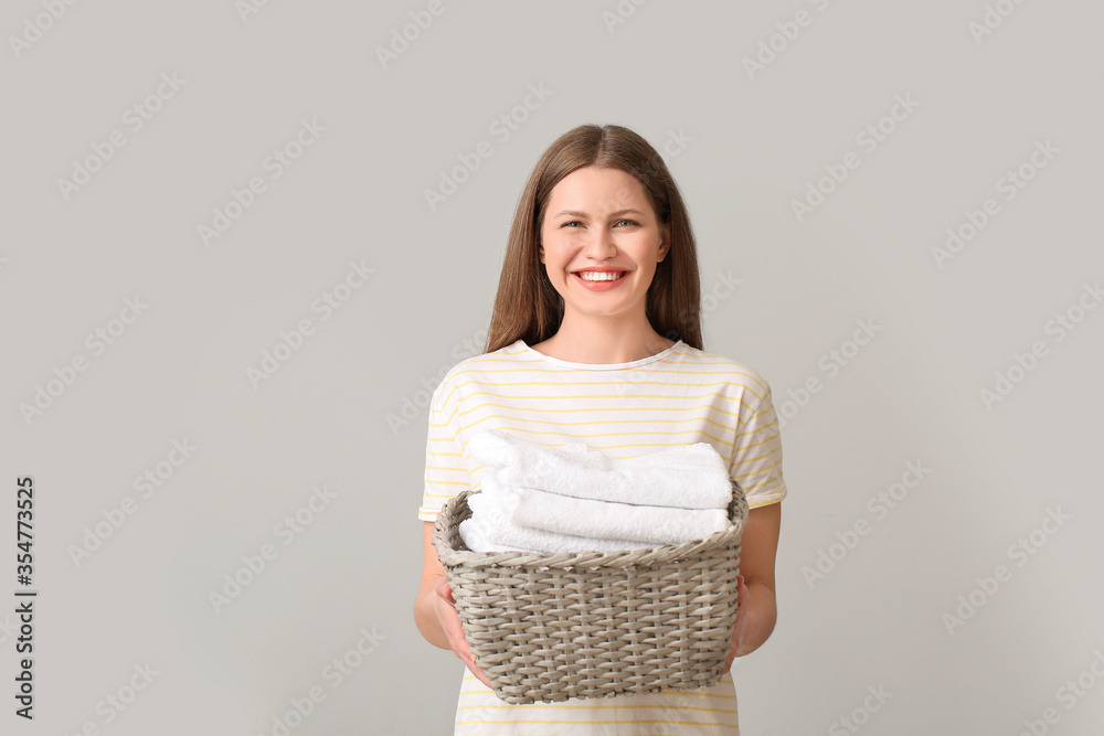 Young woman with clean laundry on grey background