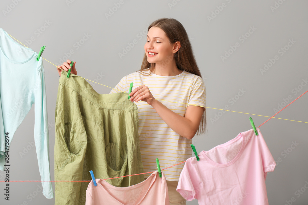 Young woman hanging clean laundry on line against grey background