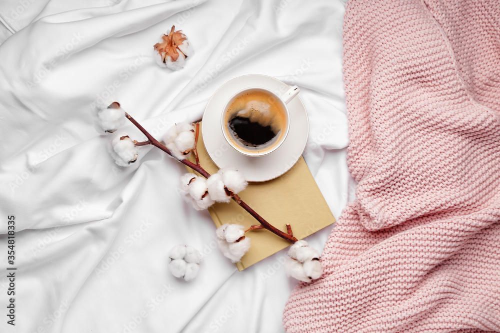 Cup of coffee, beautiful cotton branch and book on bed