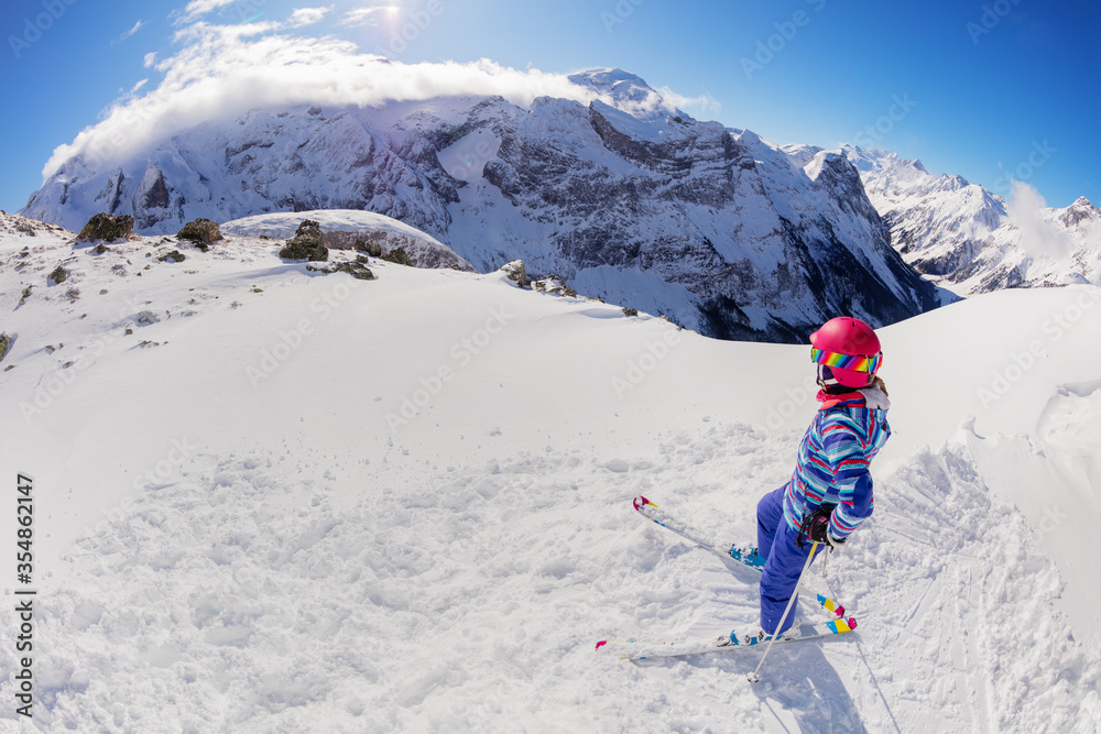 Portrait from above of a girl on ski stand in snow on top of a mountain and look down on valley wear