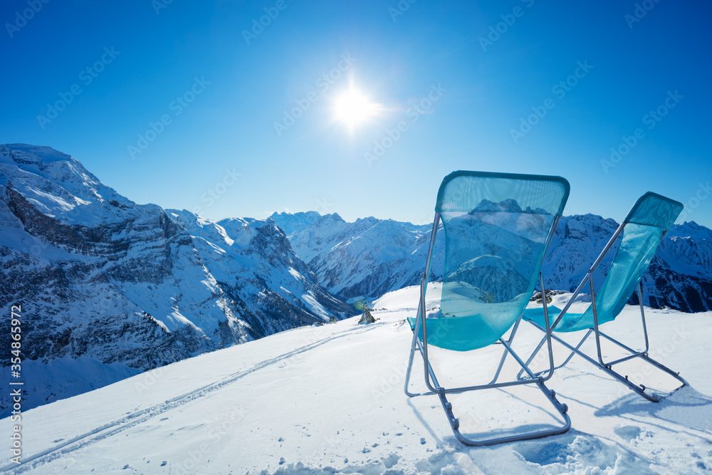 在阳光明媚的日子里，两把躺椅站在山顶的雪地上