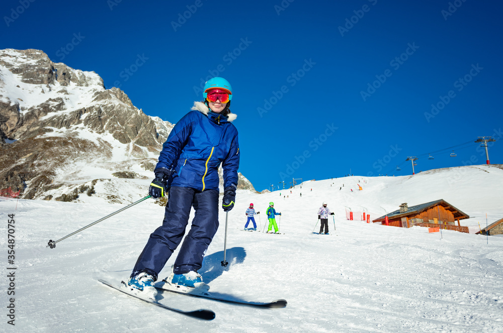 Portrait of teen girl in colorful outfit ski with kids on background on Alpine resort on sunny winte