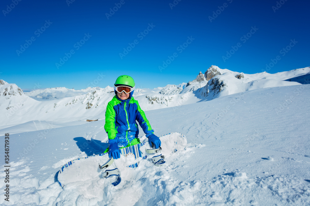 宽阔的山脉全景和可爱的微笑小男孩把滑雪板放在一边，从智慧的角度观看