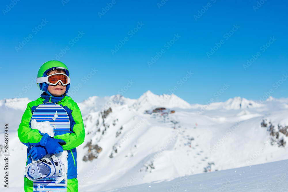 一个戴着运动头盔的男孩在阳光明媚的山顶上戴着滑雪板眼镜的近景