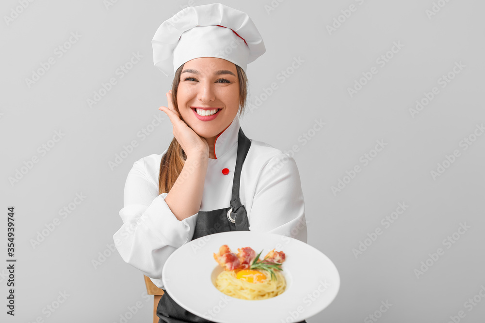 Young female chef with tasty dish on light background