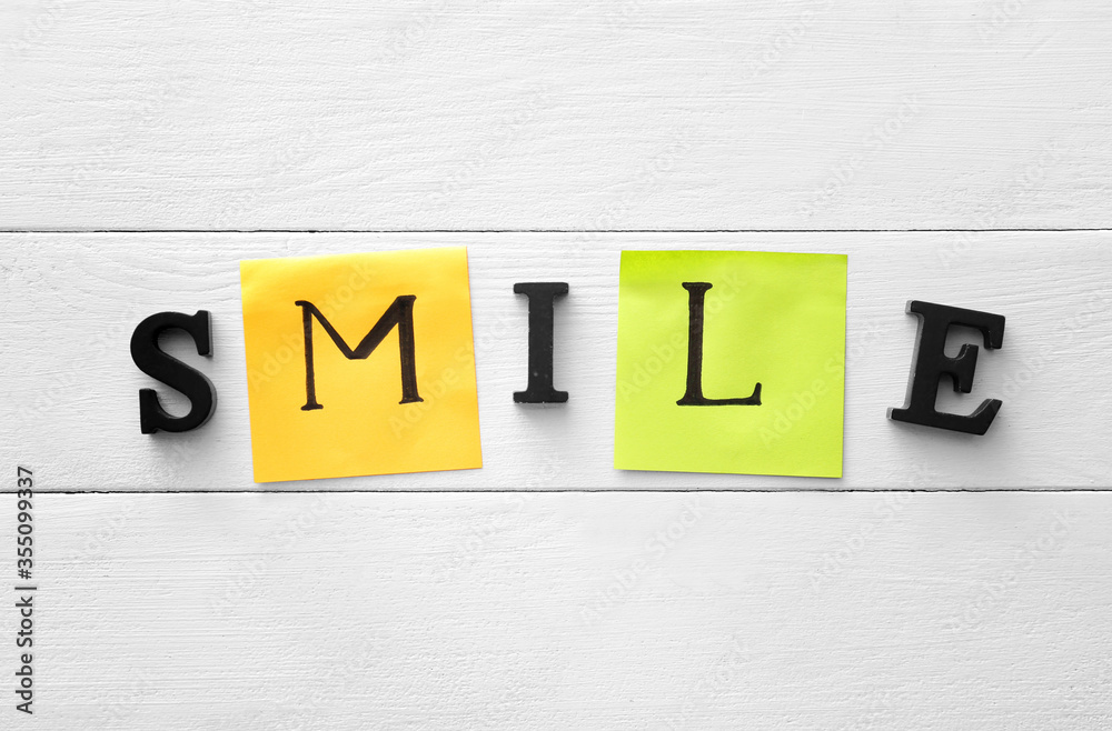 Word SMILE on white wooden background