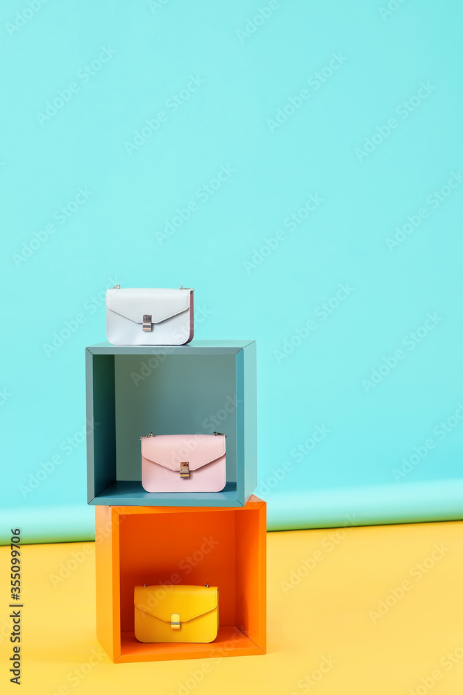 Cubes with stylish bags on color background