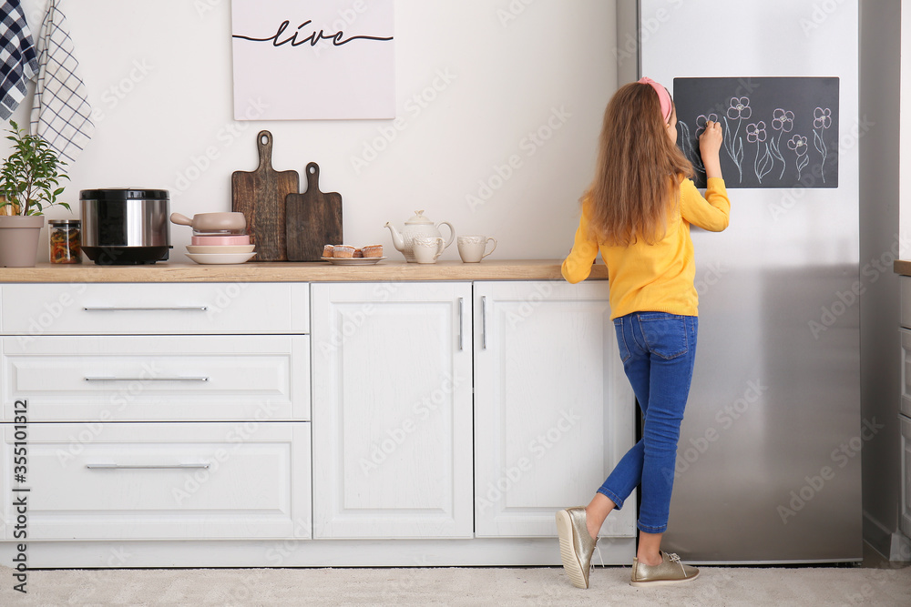 Little girl drawing on chalkboard in kitchen