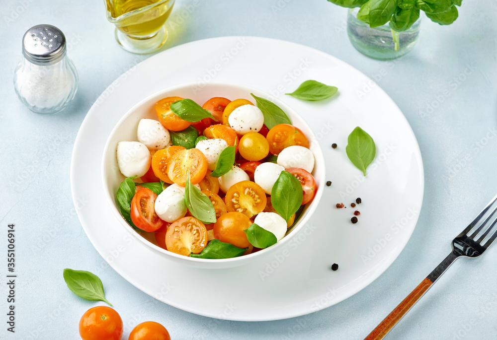 Caprese salad with tomatoes and mini mozzarella cheese in white bowl on white plate. Bocconcini mozz