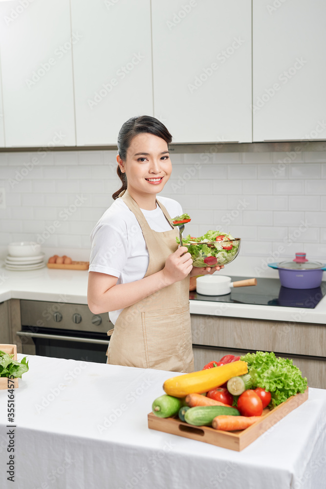 一位年轻开朗的女性在家里的厨房里吃健康沙拉的画像