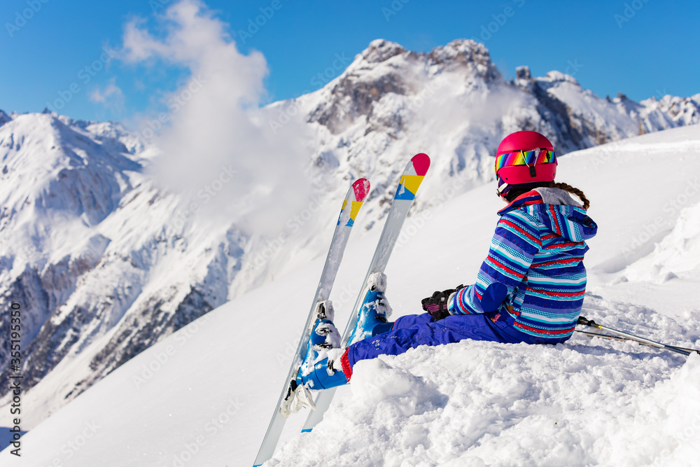 Happy young girl in bright sport outfit sit on the snow pile in the mountain over high peaks look on