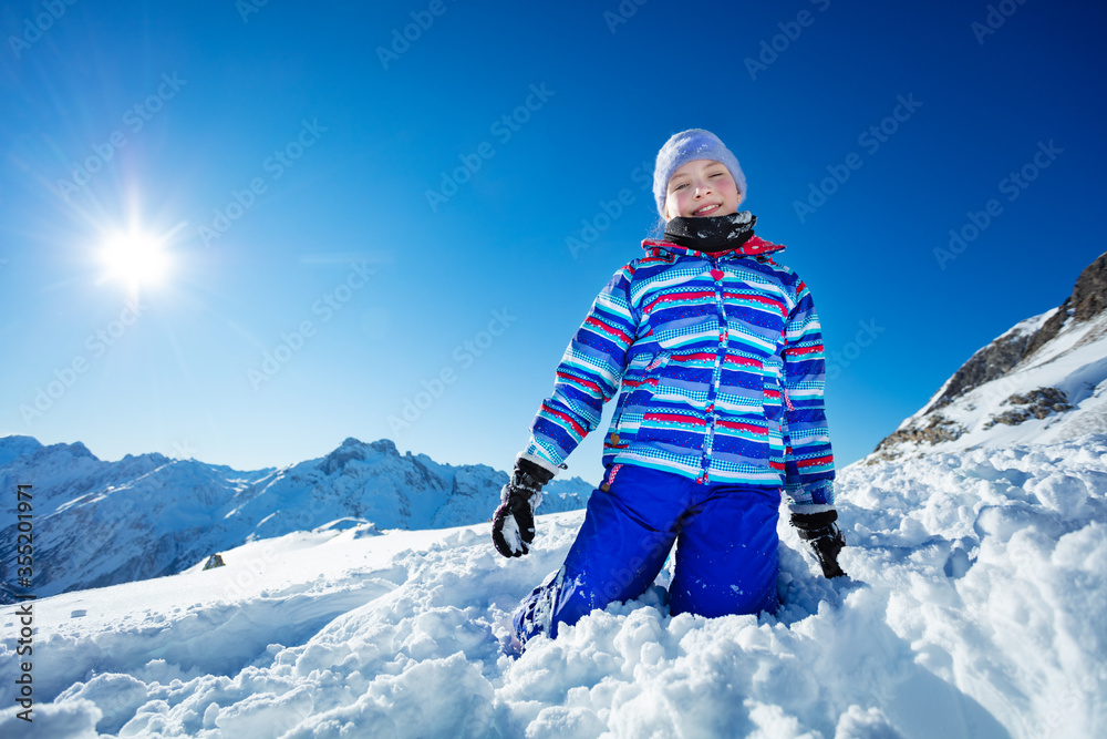 美丽女孩跪在蓝天和灿烂阳光下的雪地里的肖像