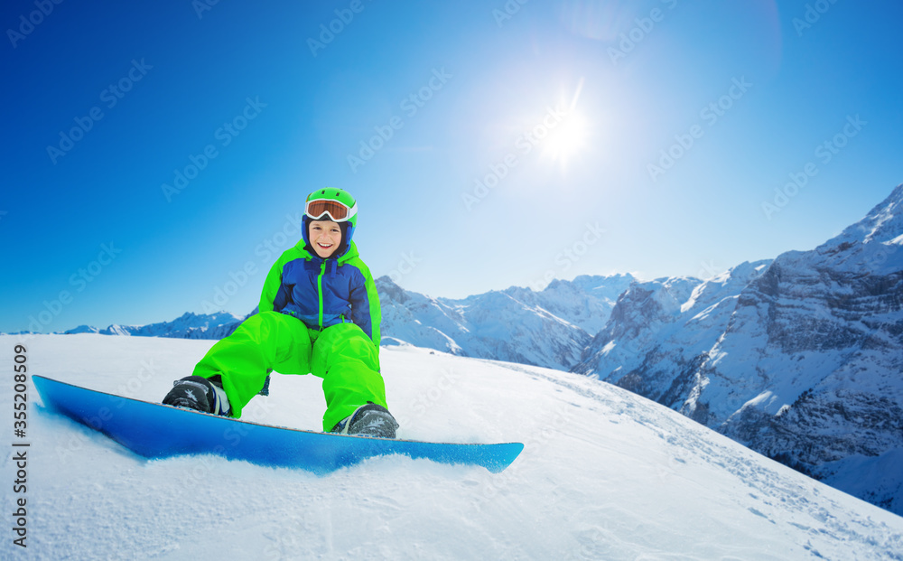 可爱的小男孩坐在滑雪板上欣赏蓝天和山脉顶部的景色