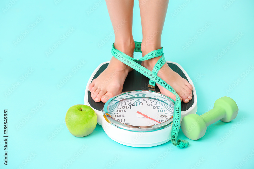 Young woman measuring her weight on color background