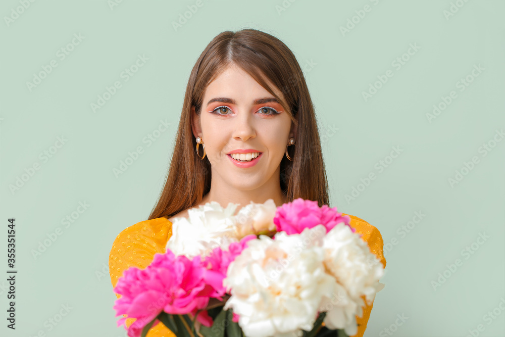 Young woman with beautiful peony flowers on color background