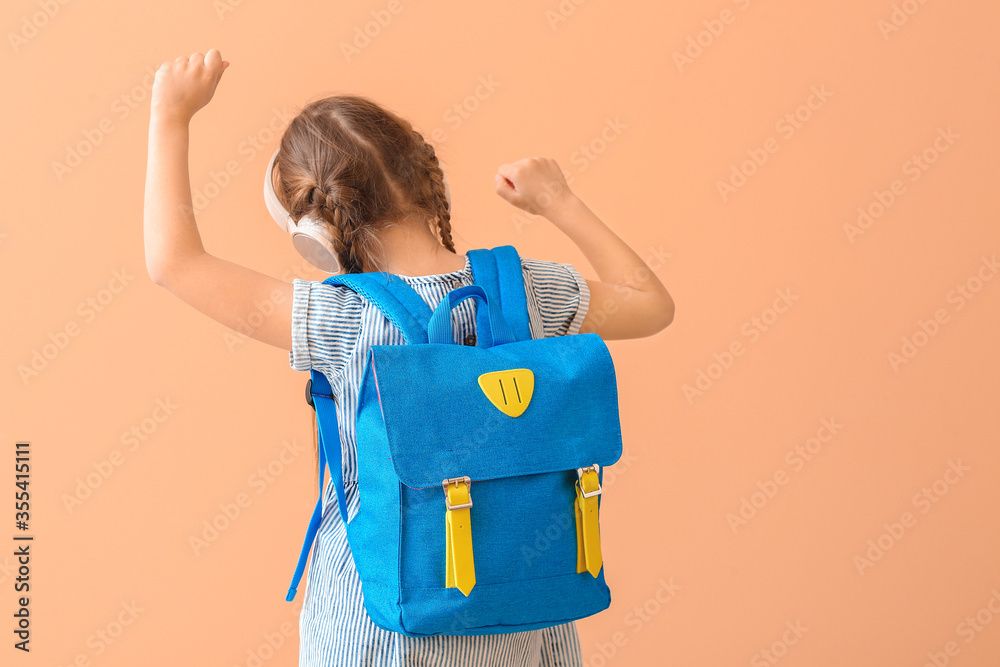 Cute little schoolgirl listening to music on color background