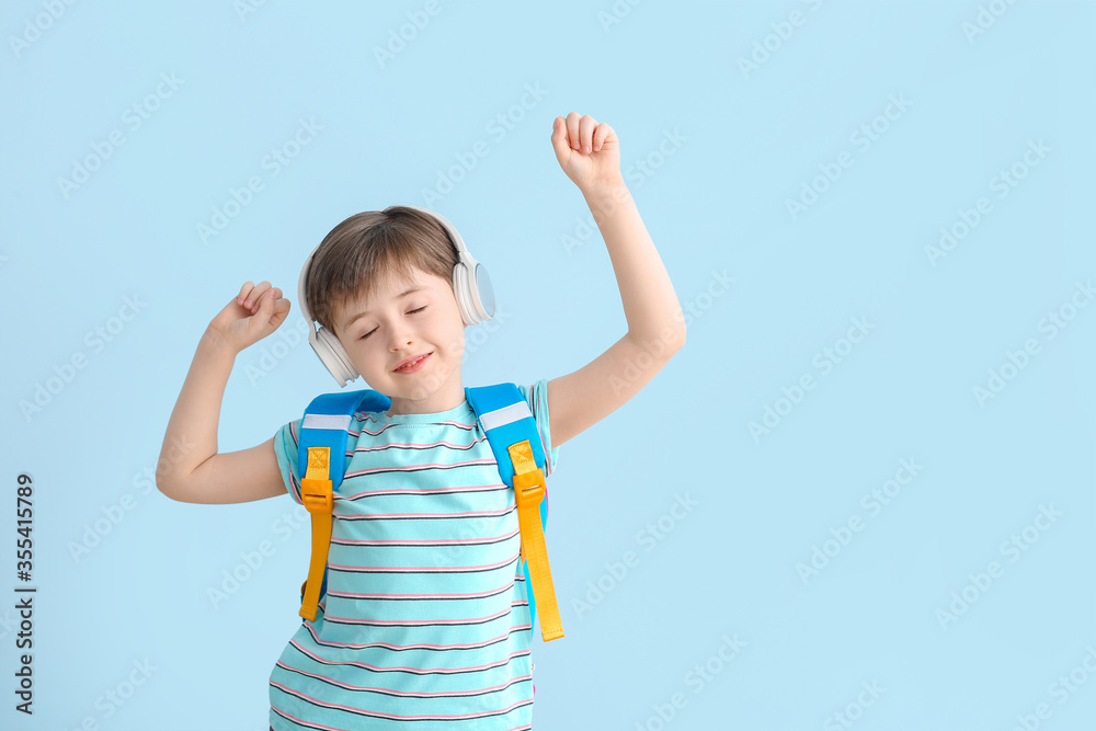 Cute little schoolboy listening to music on color background