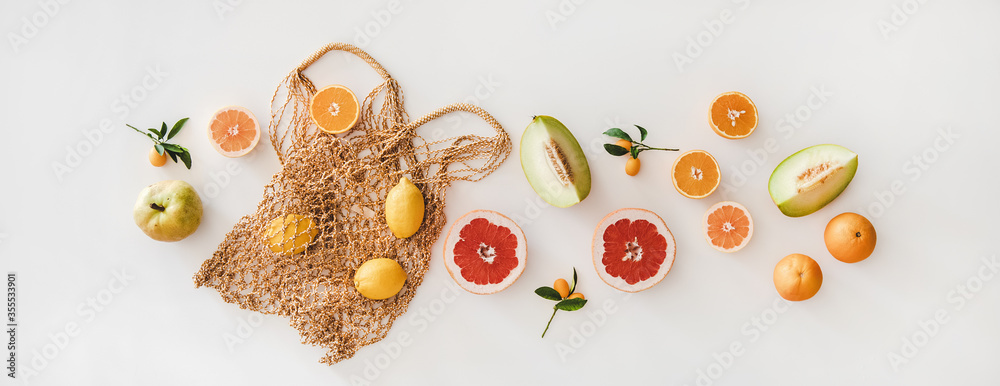 Summer mood layout. Flat-lay of summer natural net bag and various fresh fruits over white plain bac