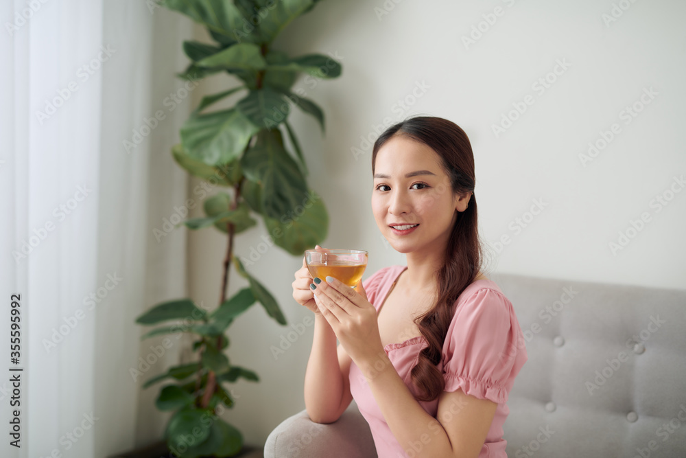 美丽的年轻亚洲女人早上在客厅喝茶。