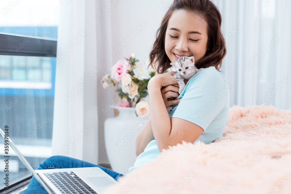 Young Asian woman working on laptop at home with kitten cat pet