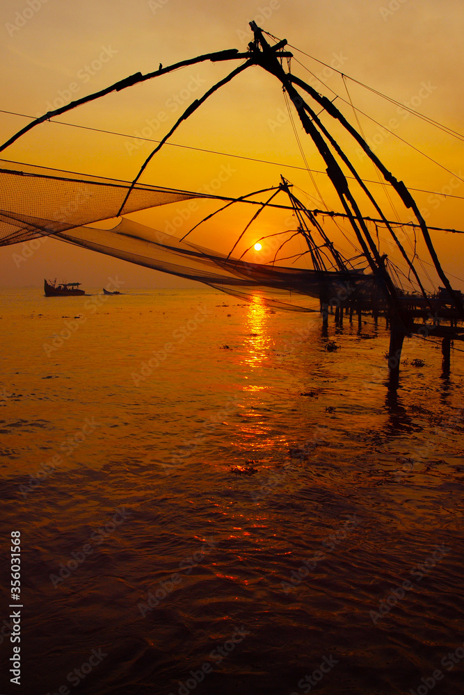 silhouette of fisherman fishing with large net during sunset in cochin - india 