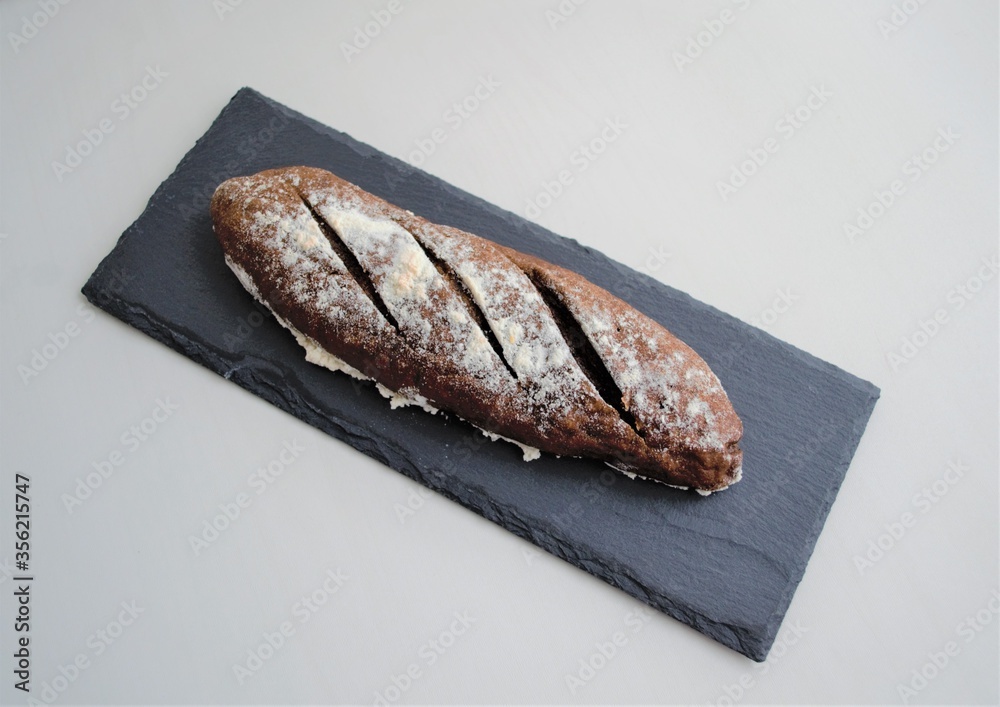 Homemade french rye mini baguette on a slate board, on a light background