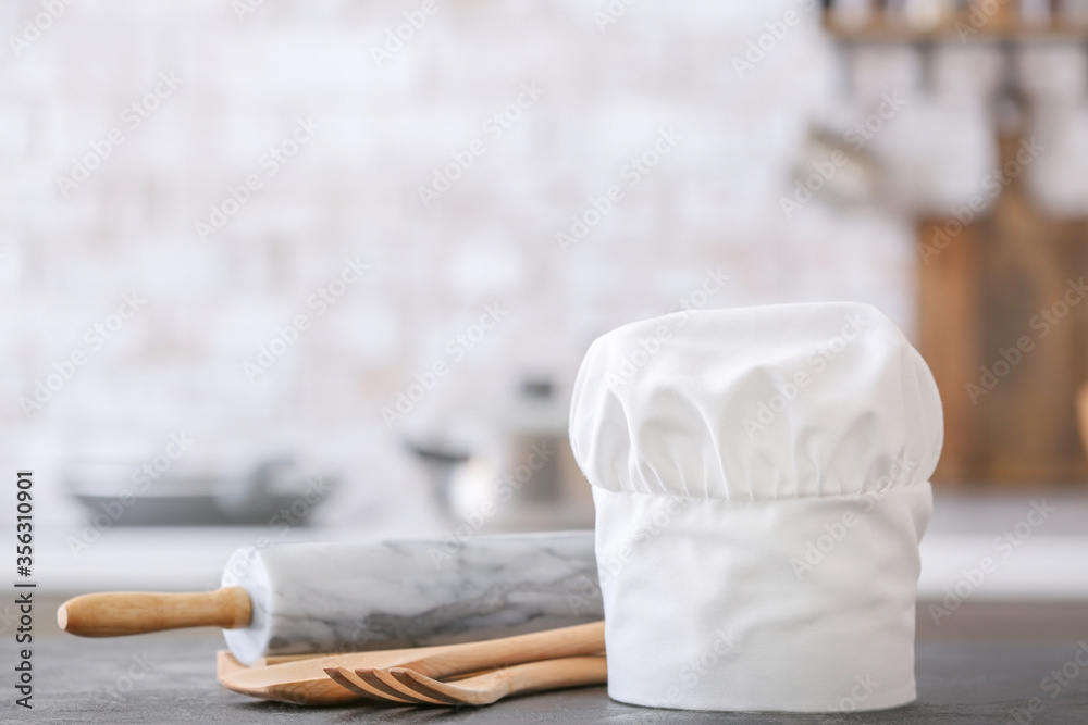 Chef hat and utensils on table in kitchen