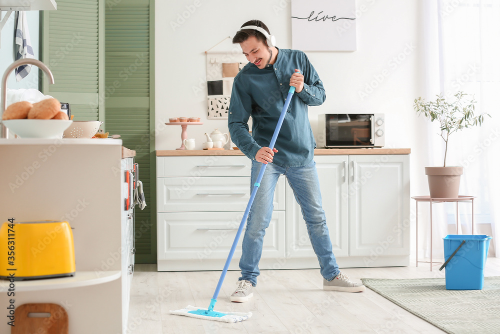 Handsome young man mopping floor in kitchen