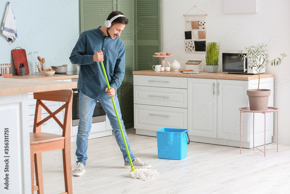 Handsome young man mopping floor in kitchen