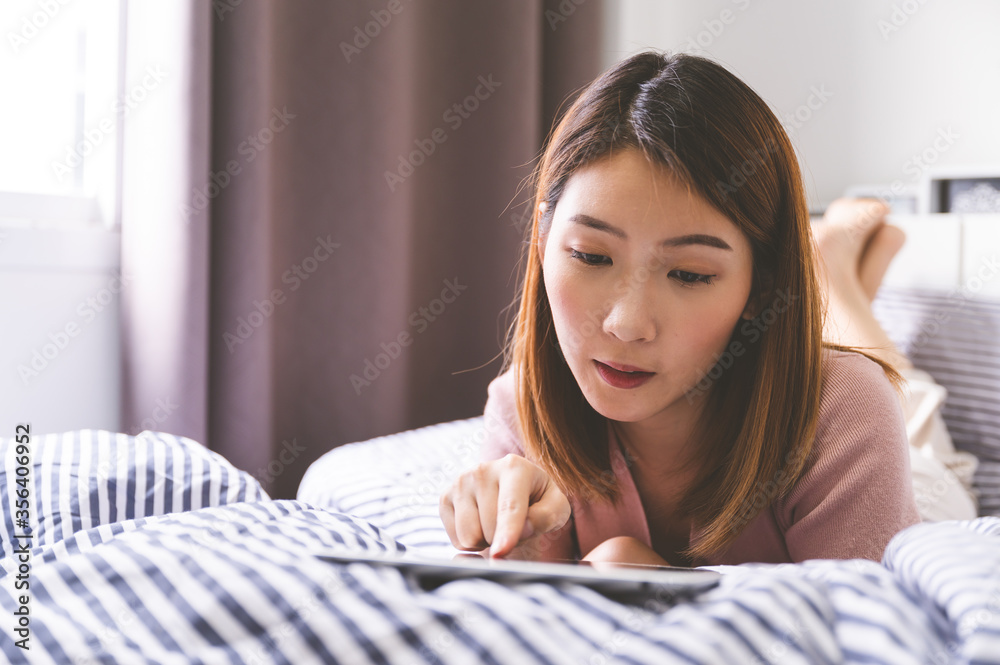 Young asian woman using tablet on bed. concept of browsing internet, reading, learning, online shopp