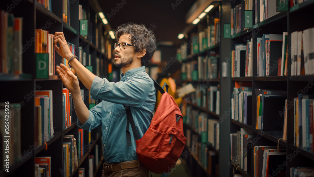 大学图书馆：聪明的西班牙裔男孩的画像站在一排排书架之间寻找