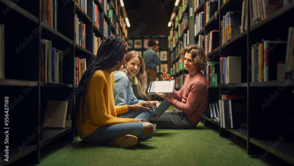 大学图书馆：一群不同的学生盘腿坐在地板上，交谈，使用数字T