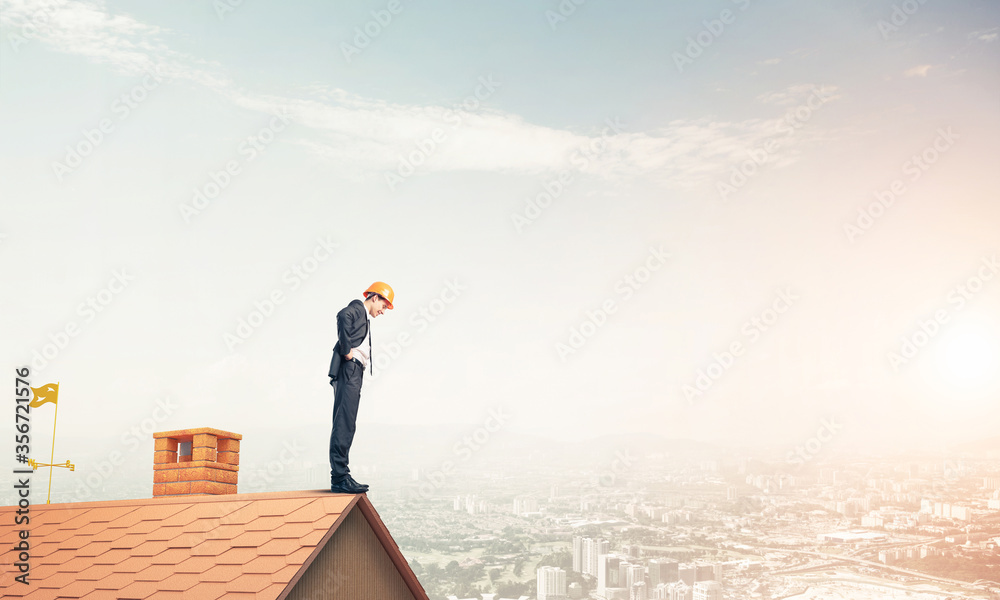 Businessman looking down from roof and modern cityscape at backg