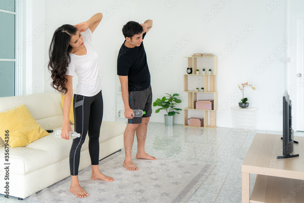 年轻的亚洲夫妇一起进行高强度间歇训练，在家看电视，男人和女人