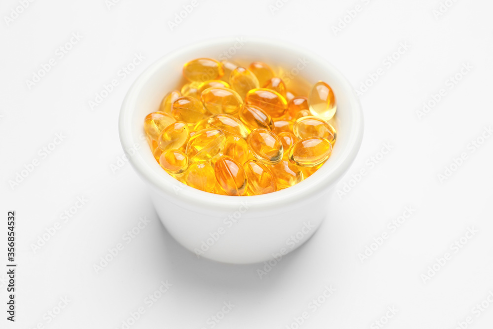 Bowl with fish oil capsules on white background