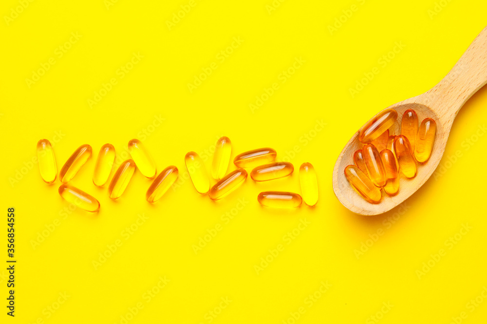 Spoon with fish oil capsules on color background