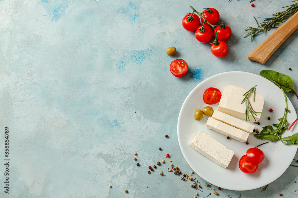 Tasty feta cheese with olives, tomato and spices on color background