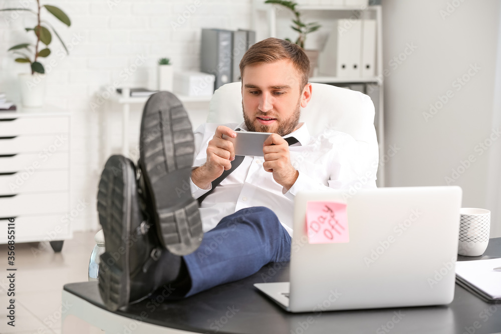 Lazy young businessman with mobile phone relaxing in office