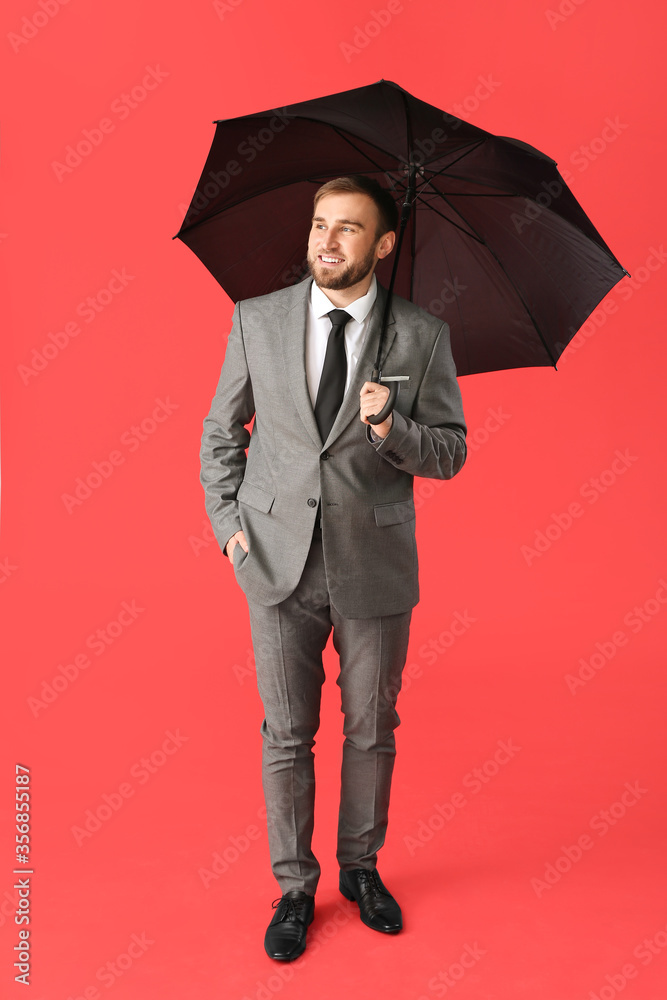 Handsome businessman with umbrella on color background