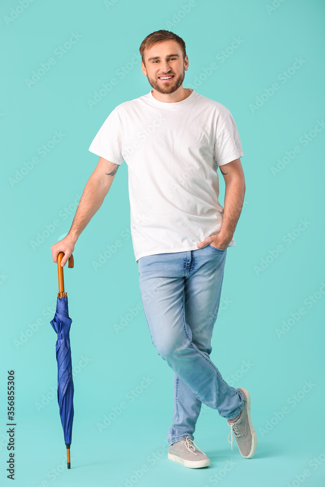 Handsome young man with umbrella on color background