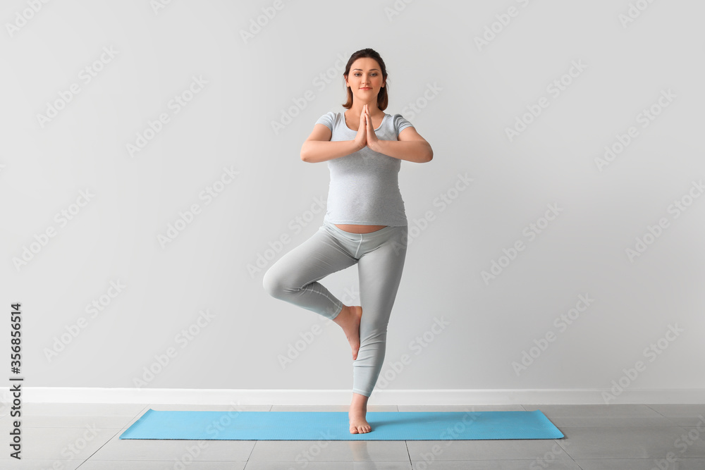 Young pregnant woman practicing yoga near light wall