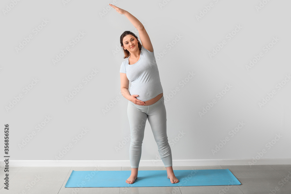 Young pregnant woman practicing yoga near light wall