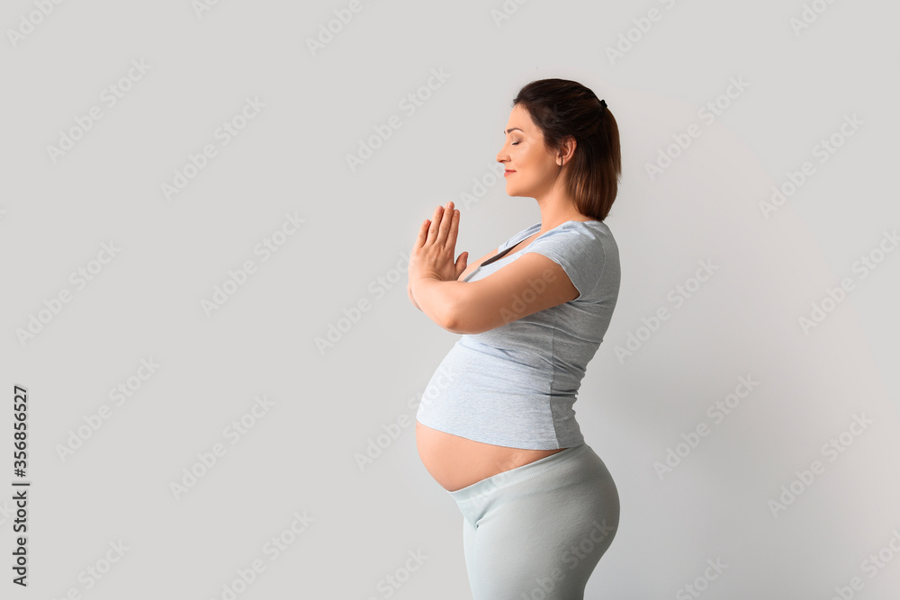 Young pregnant woman practicing yoga near light wall